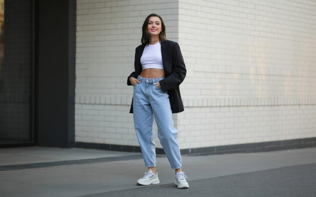 Woman wearing stylish baggy jeans outfit with fitted white top and chunky sneakers against brick wall