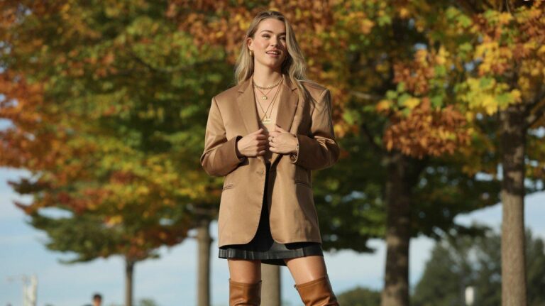 Stylish woman in oversized camel blazer and mini skirt outfit standing among autumn trees