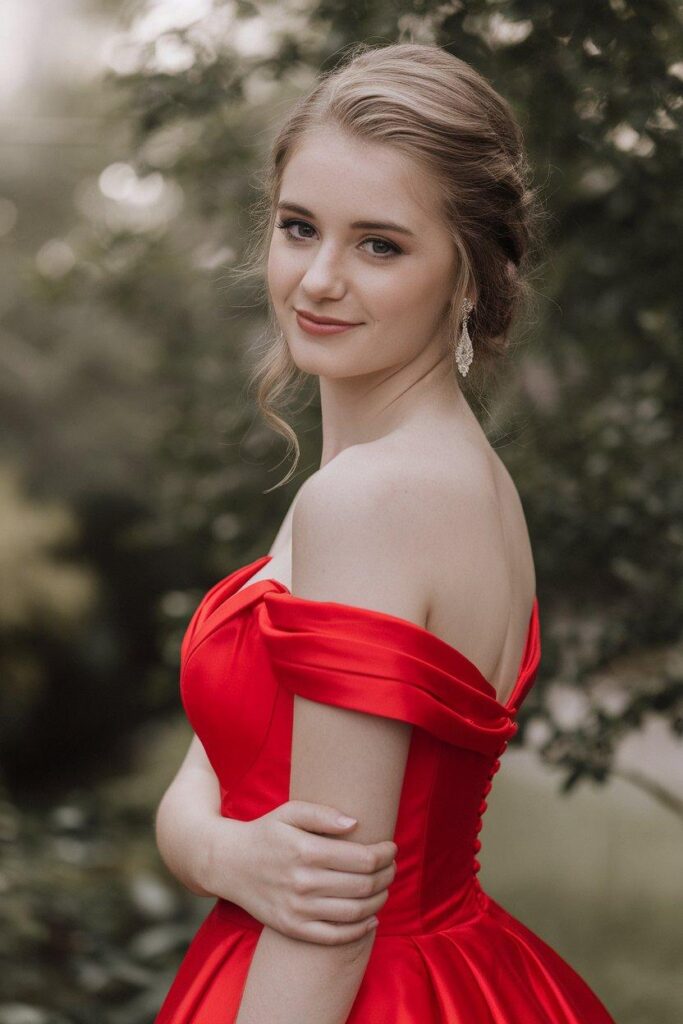 Red off-shoulder prom dress highlighting elegant neckline in garden setting