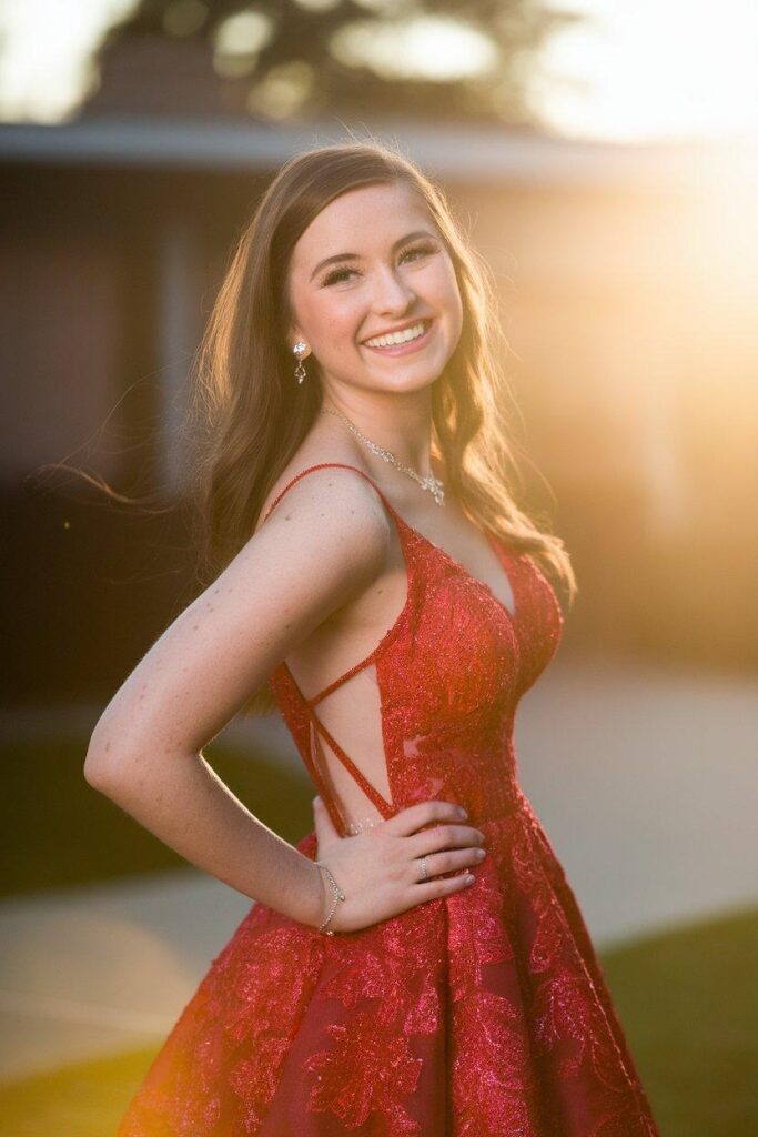Confident young woman in red prom dress with joyful smile and empowering pose