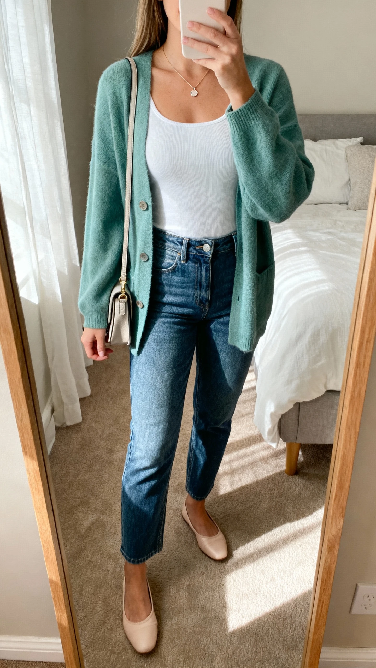 iPhone mirror selfie of a woman wearing a soft cardigan (sage) over a fitted white cami, high-rise straight jeans, ballet flats, dainty pendant, small crossbody bag, face not visible, bedroom mirror with afternoon light, natural iPhone photo quality.