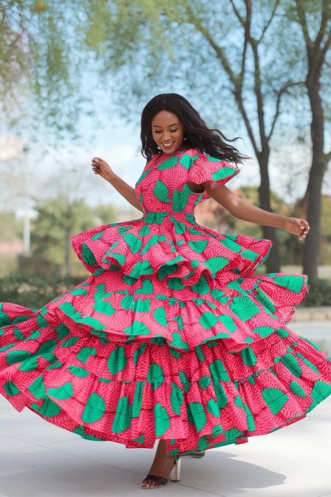 Woman twirling in layered frill Ankara dress with pink and green prints