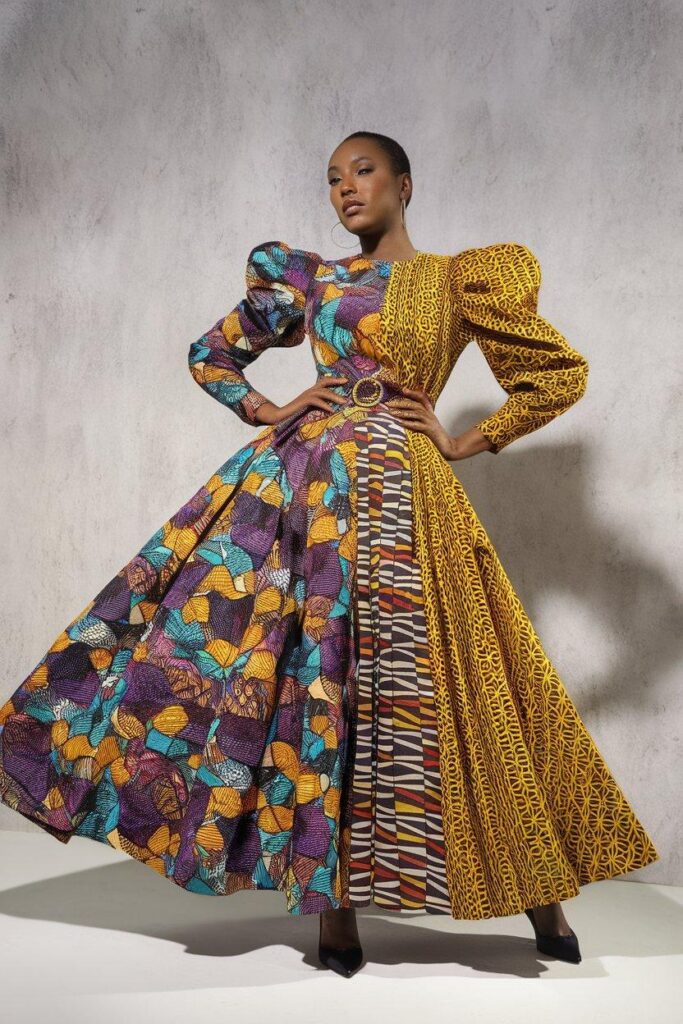 Woman posing in colorful mixed-print Ankara dress against simple wall