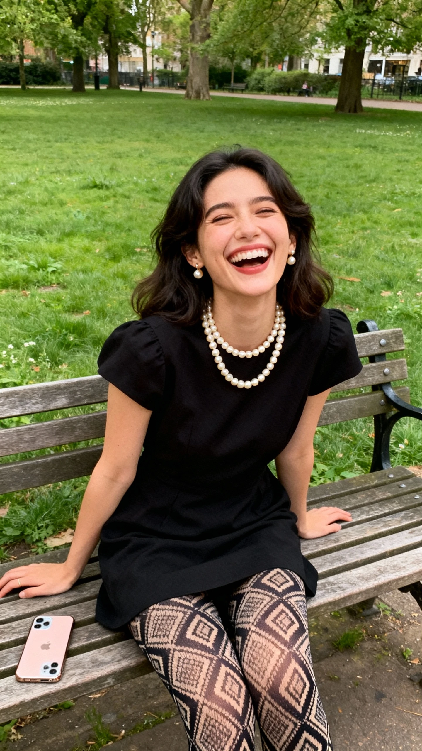 A woman in a little black dress with statement patterned tights and pearl accessories, laughing on a park bench, casual iPhone photo style, natural daylight, outdoor setting.
