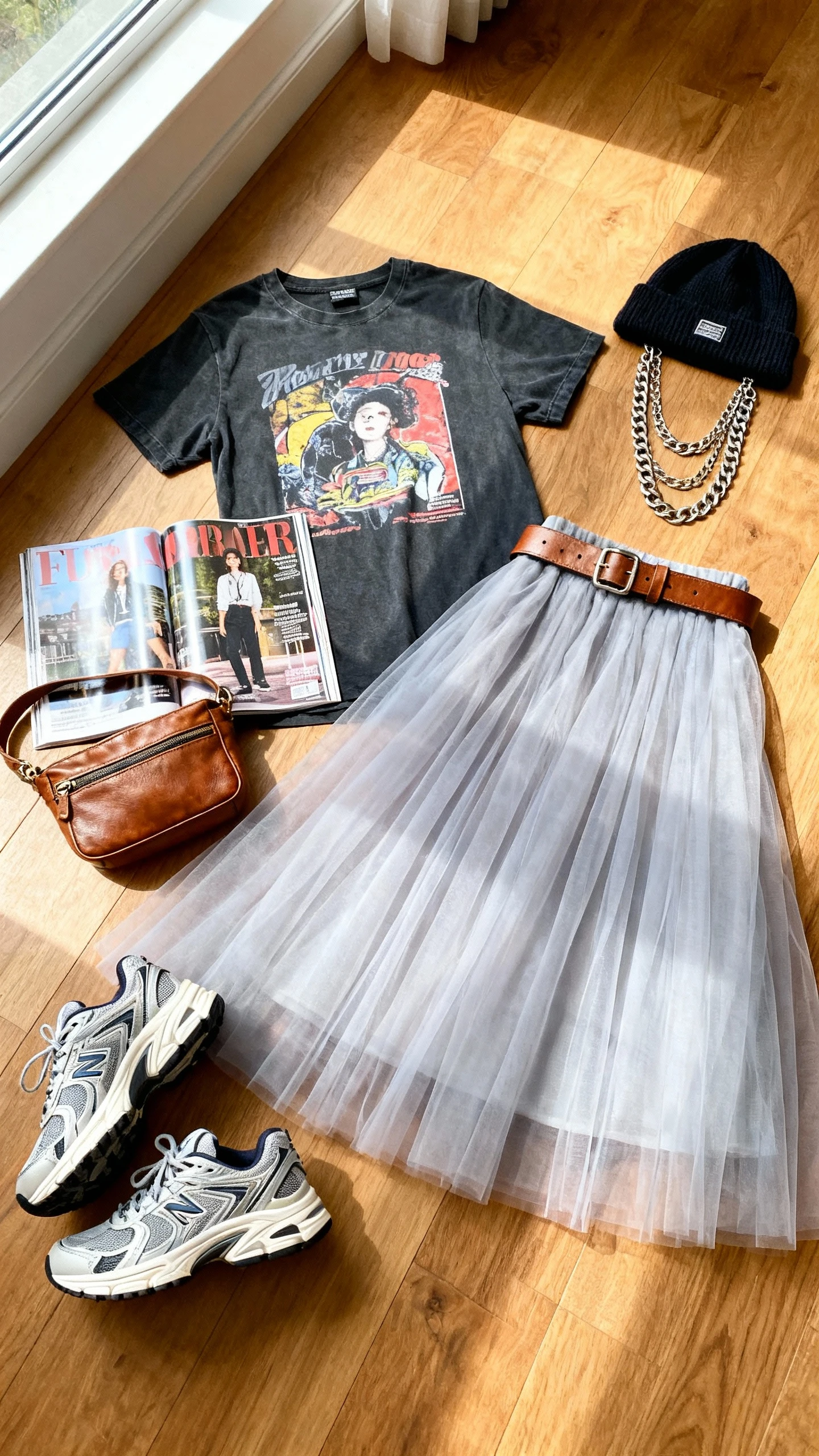 Flat lay overhead of modern tulle midi skirt, graphic tee, leather belt bag, chunky sneakers, layered chain necklaces, and a beanie on wooden floor; include a glossy magazine prop, bright natural window light, no person visible, organized composition, iPhone photo aesthetic.