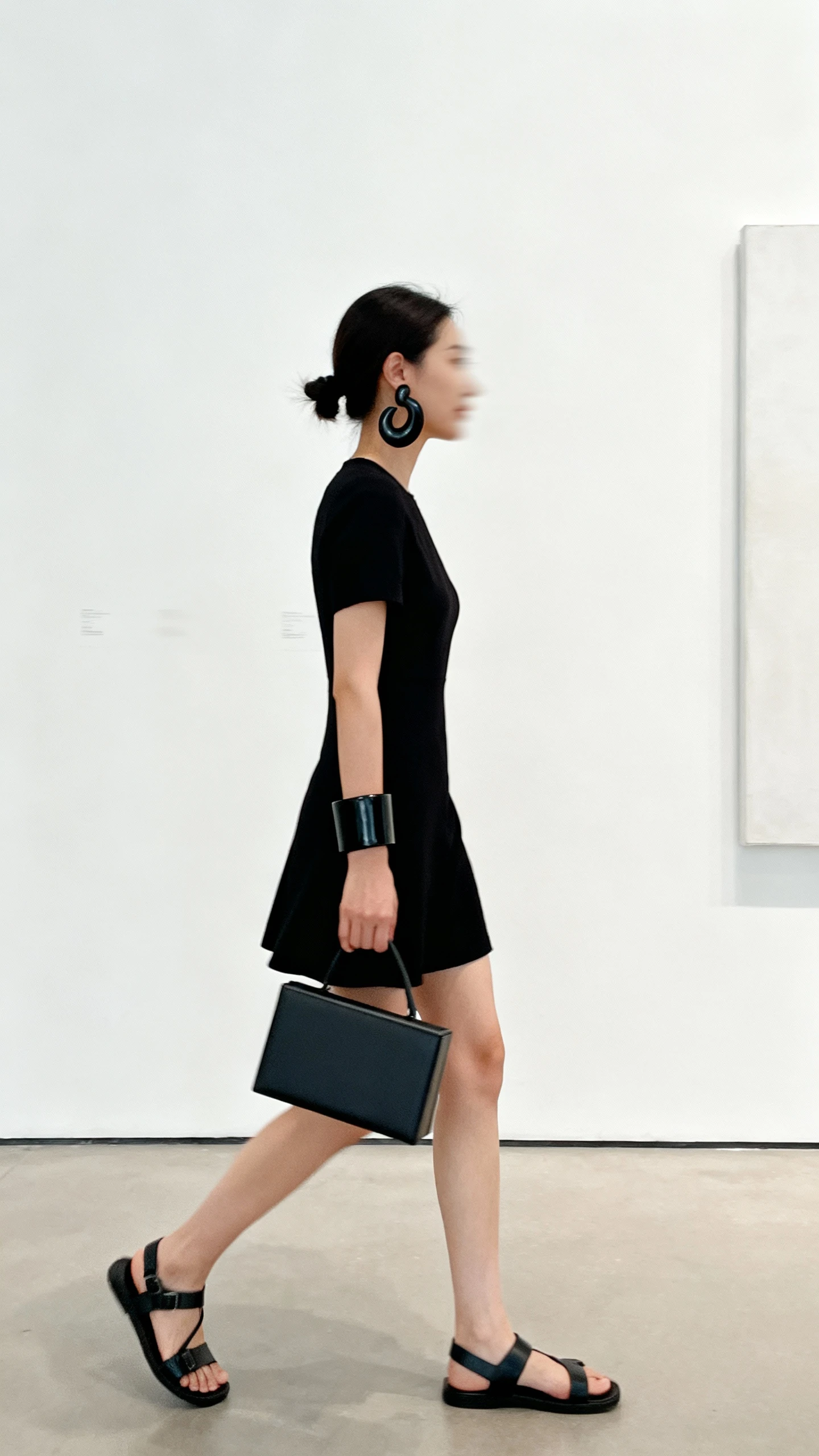 Minimalist candid photo of a woman in a little black dress styled with black sculptural earrings, a structured black cuff, sleek black sandals, and a clean boxy bag, walking past a white gallery wall, face slightly blurred, soft daylight, iPhone photo quality.