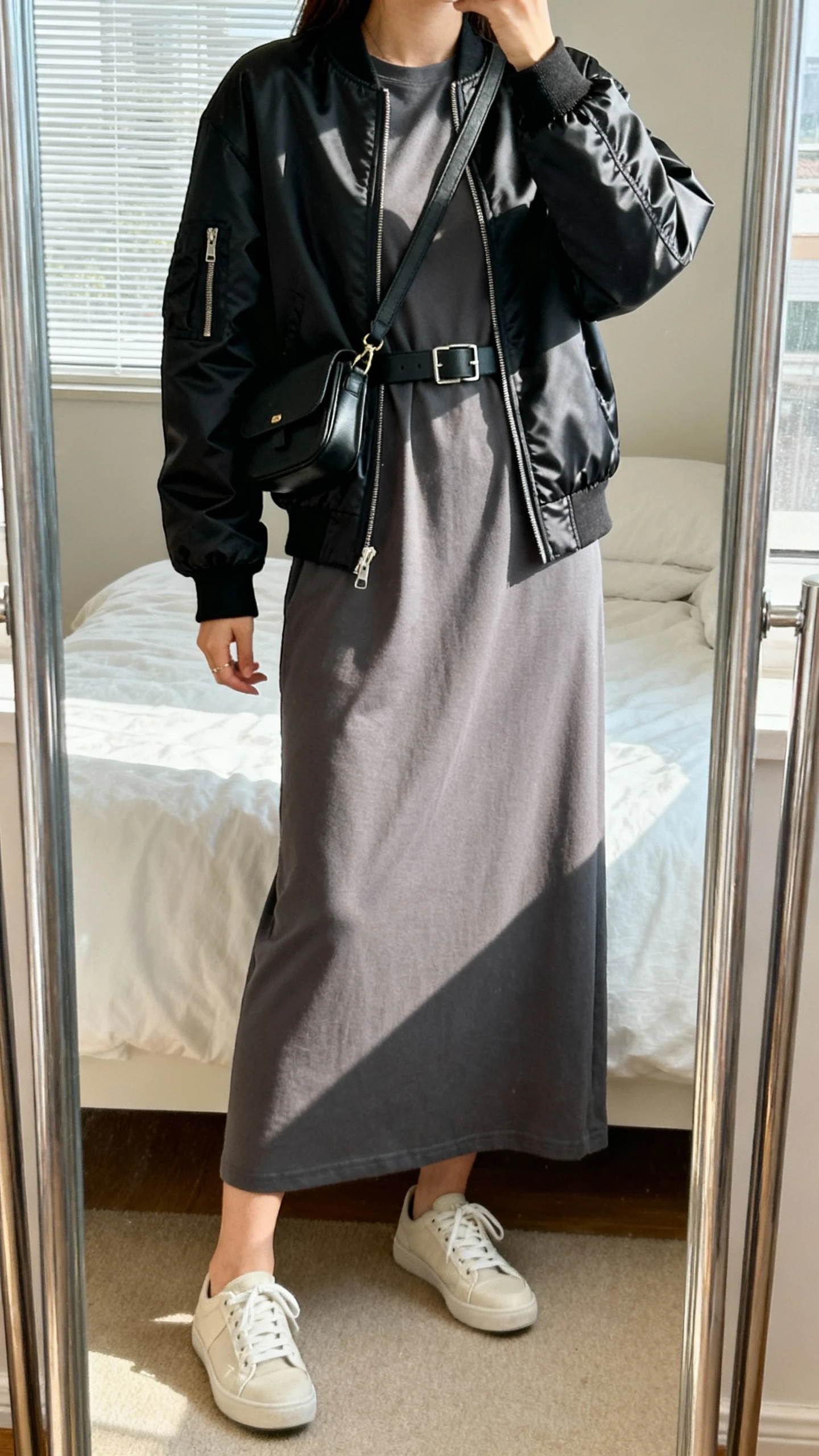 iPhone mirror selfie of a woman in a long T-shirt dress topped with a sleek bomber jacket, minimalist sneakers, crossbody belt bag, face not visible, cropped at shoulders, bedroom full-length mirror with soft window light, iPhone photo quality.